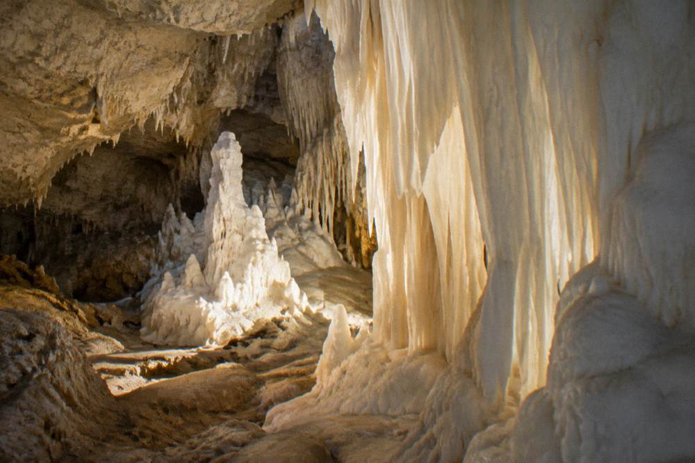 A chamber of pure white alabaster formations glowing under soft light, delicate curtains and spires of white stone, no people, Grotte di Castellana