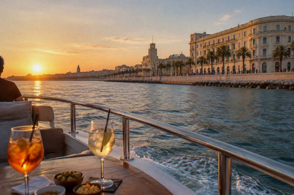A boat cruising along the seafront with the curve of cream monumental buildings and palm trees on shore, passengers far off, aperitif glasses on a table, Lungomare Nazario Sauro