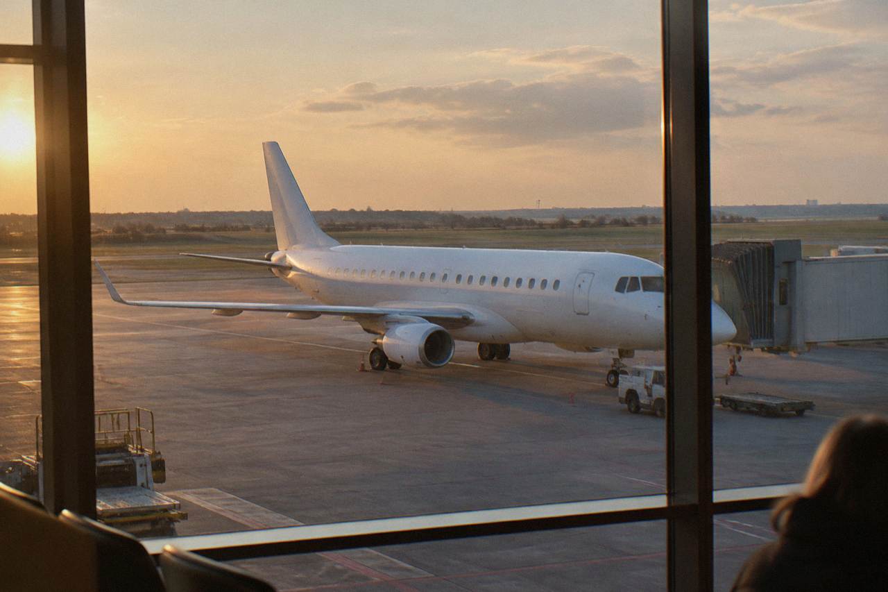 Regional jet parked on an apron seen through a terminal window with a plain white fuselage