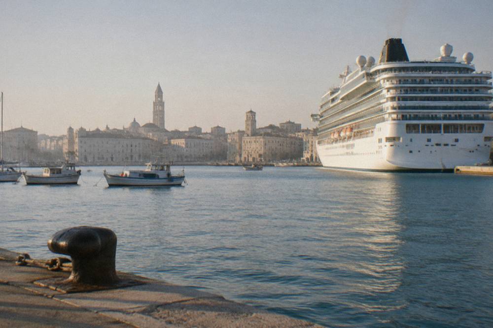 Cruise ship docked beside the pale old town skyline with two towers and small boats in front