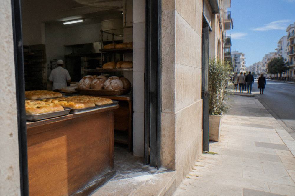Neighbourhood bakery doorway with trays of golden focaccia and round loaves seen from the street