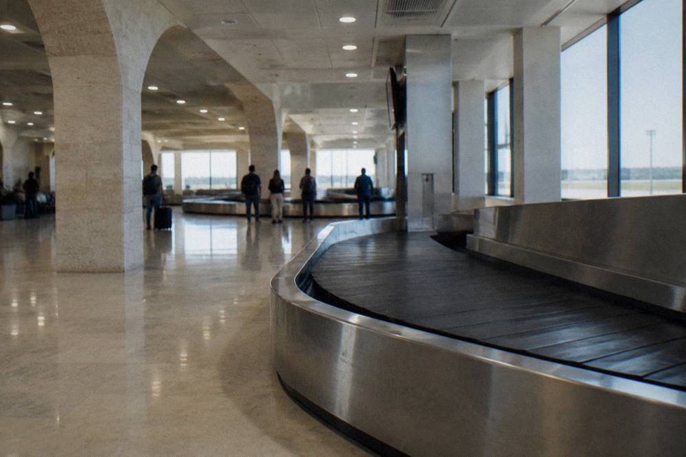 Baggage reclaim hall with an empty belt curving through and a few travellers watching far off