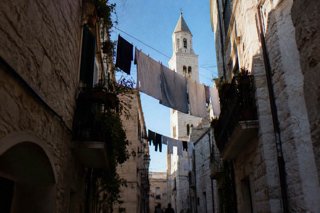 Looking up between close walls at a strip of blue sky crossed by washing lines and a bell tower