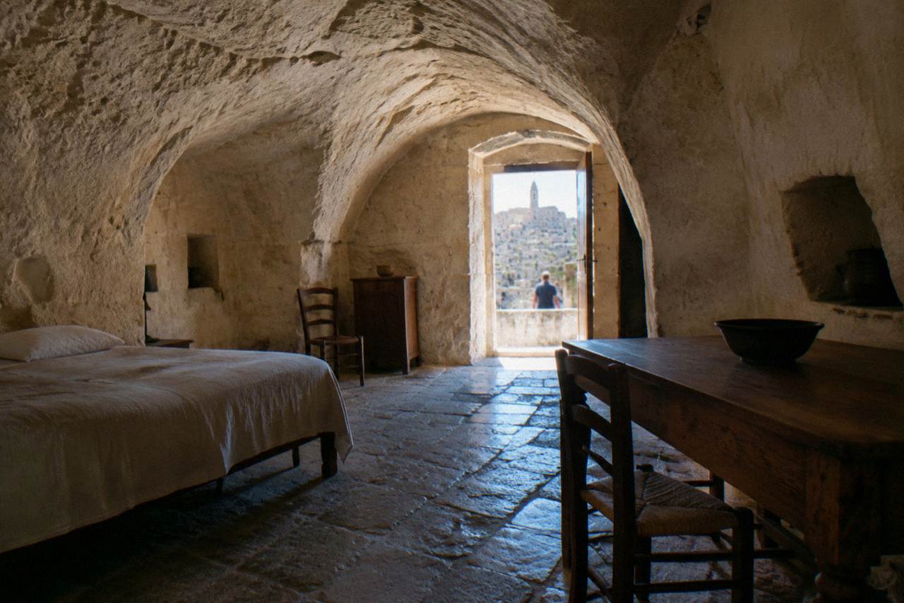 Inside a restored cave dwelling with an arched rock ceiling, a simple bed and a wooden table