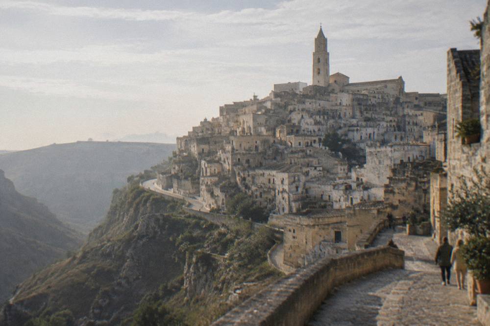 Tiers of honey-coloured cave dwellings stacked on the side of a deep ravine below a cathedral bell tower