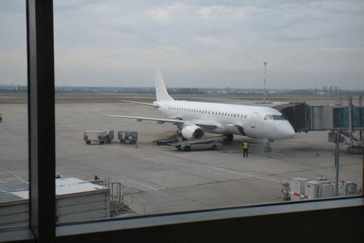 Regional jet parked on an apron seen through a terminal window with a plain white fuselage