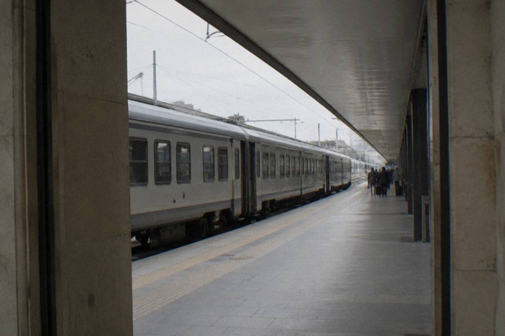 Regional train pulling into a station platform under a long canopy with a few distant waiting travellers