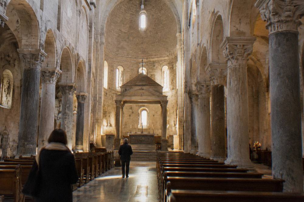Long stone nave of a Romanesque basilica with simple columns and a raised sanctuary in soft window light