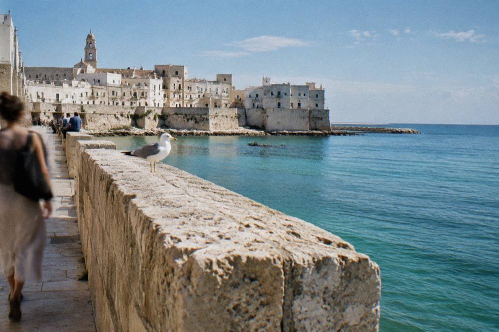 Sea promenade along an old town wall above calm turquoise water with distant people sitting on the wall
