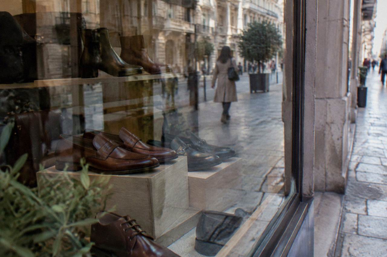 Shop window with leather shoes behind glass reflecting the street and a blurred passer-by