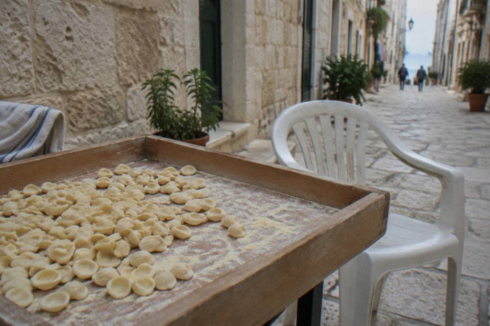 Tray of small ear-shaped orecchiette dusted with semolina on a wooden table beside a plastic chair