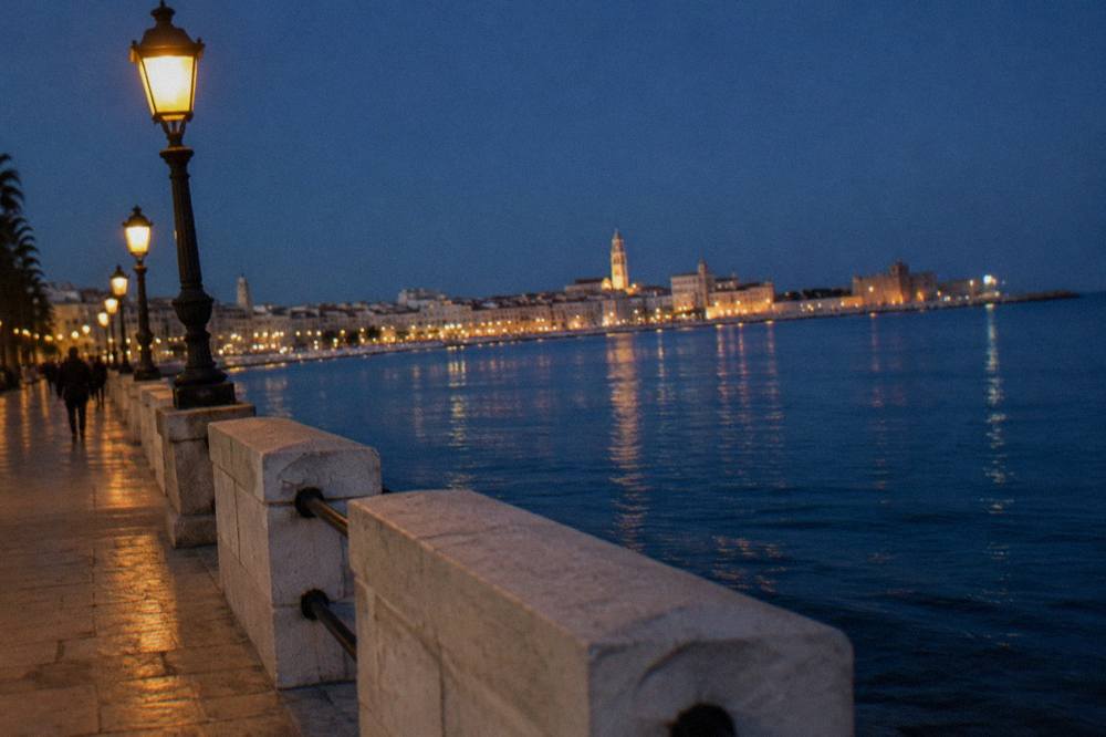 Seafront promenade at blue hour with lit street lamps and the lights of the old town across the bay