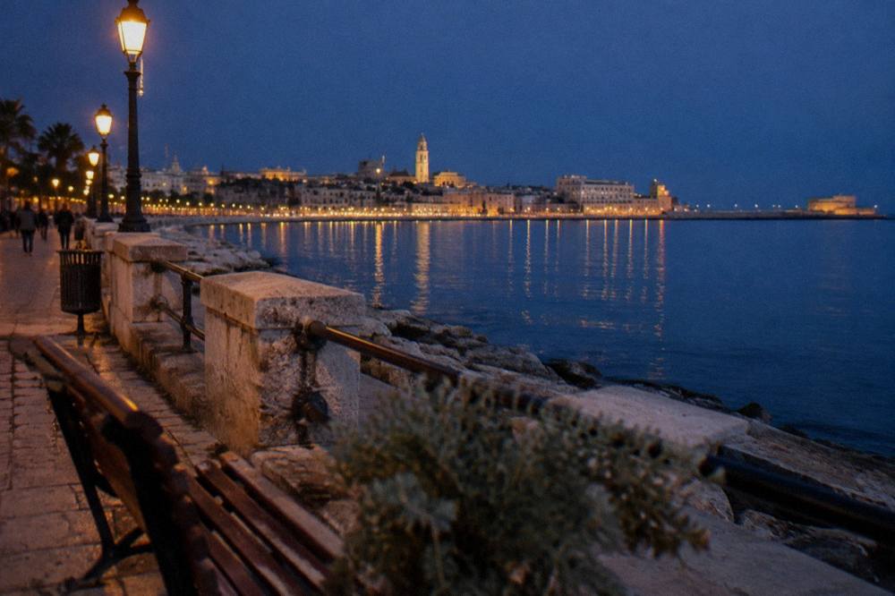 Seafront promenade at blue hour with lit street lamps and the lights of the old town across the bay