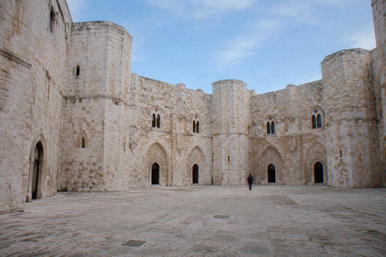 Octagonal inner courtyard of a medieval castle with arched doorways in pale stone and a blue sky