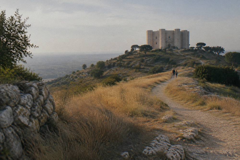Dusty path winding up a hill through dry grass towards a distant pale octagonal castle in late afternoon