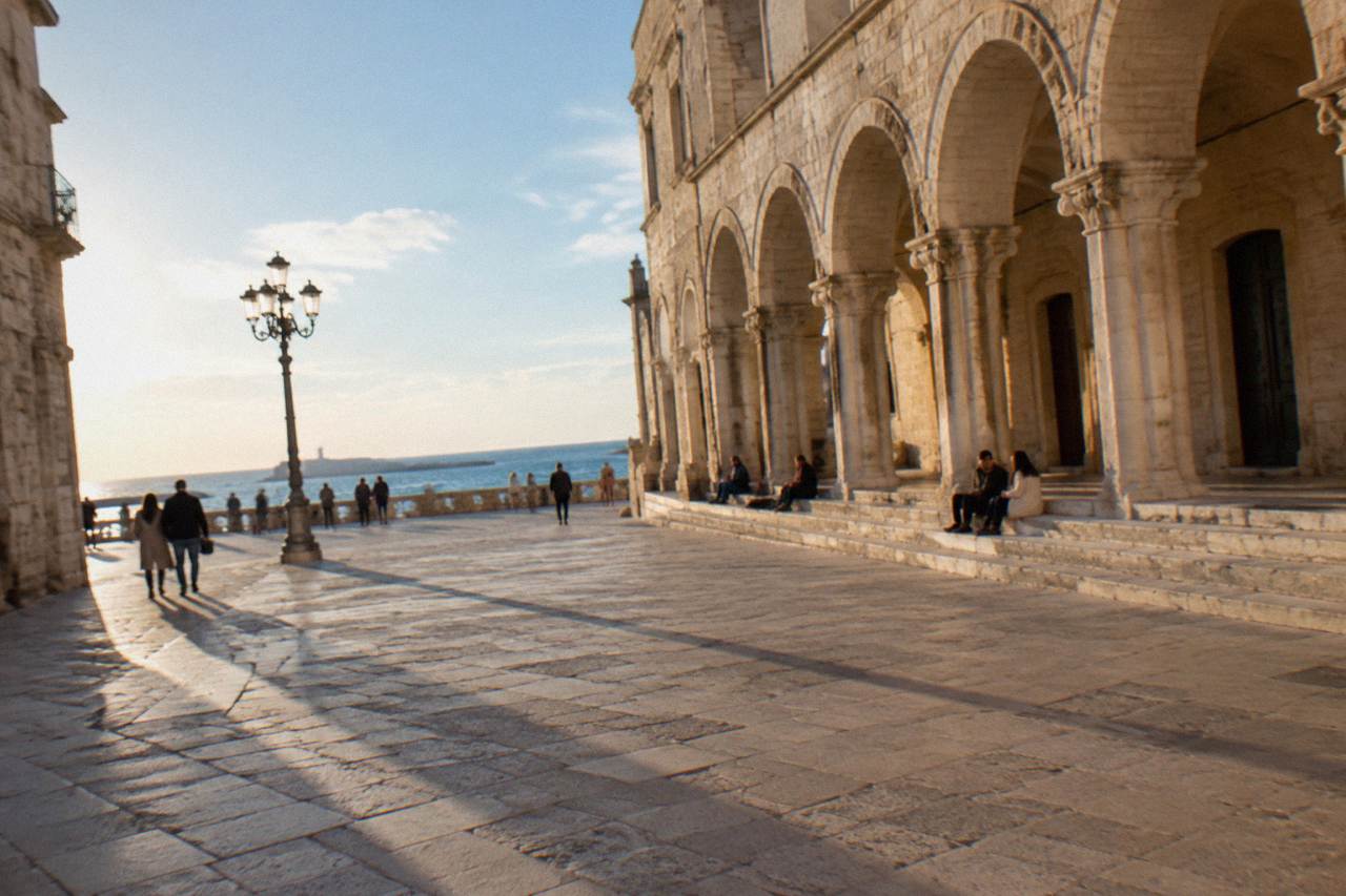 Loggia arches with long afternoon shadows and a few distant people sitting on the steps