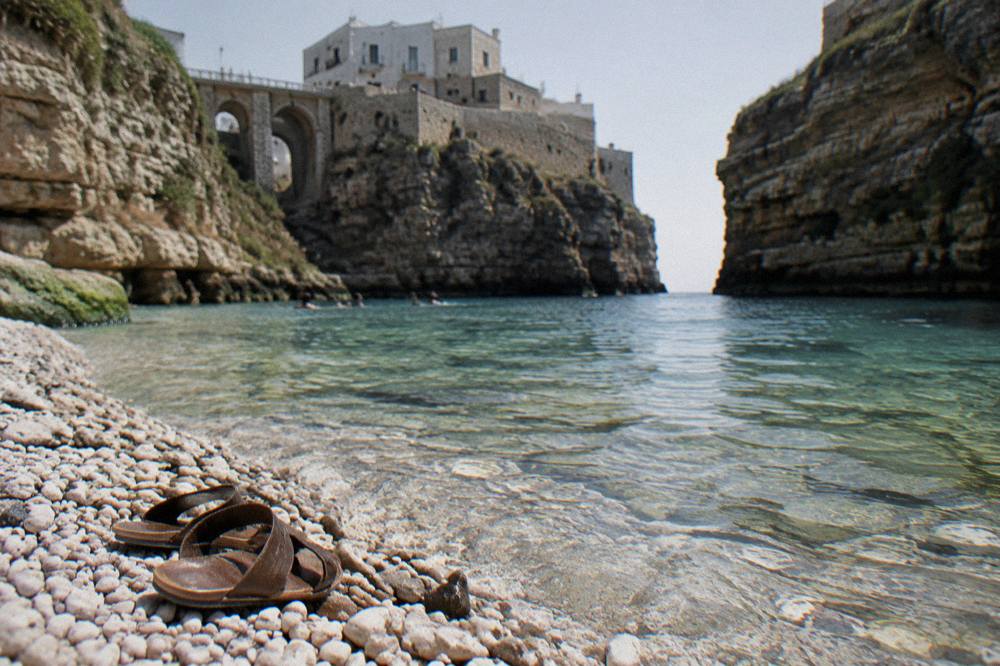White pebbles and clear shallow water at the edge of a cove with a pair of sandals left on the stones