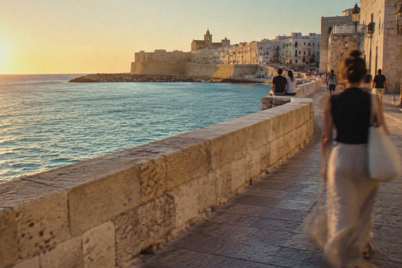 Sea promenade along an old town wall above calm turquoise water with distant people sitting on the wall