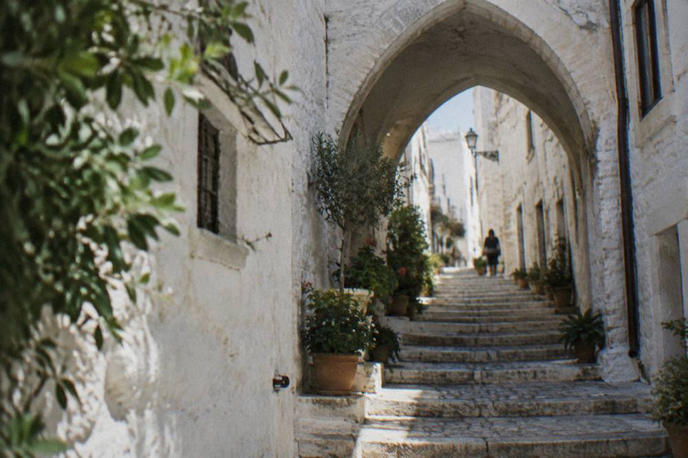 Steep whitewashed alley with stone steps, a pointed arch overhead and potted plants