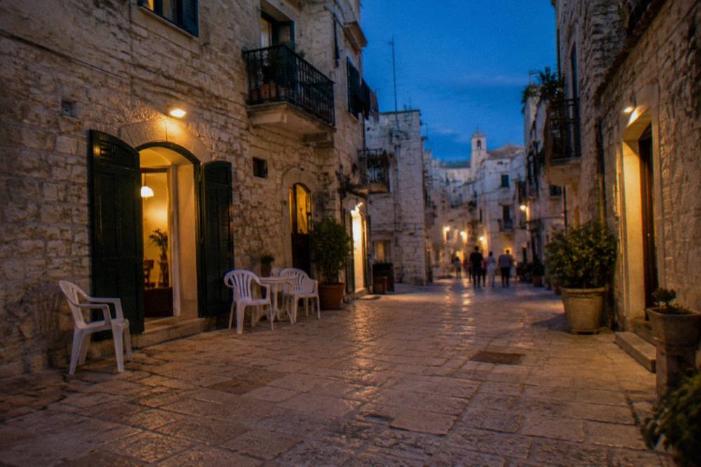 Old town lane at blue hour with warm light glowing from doorways and chairs set outside