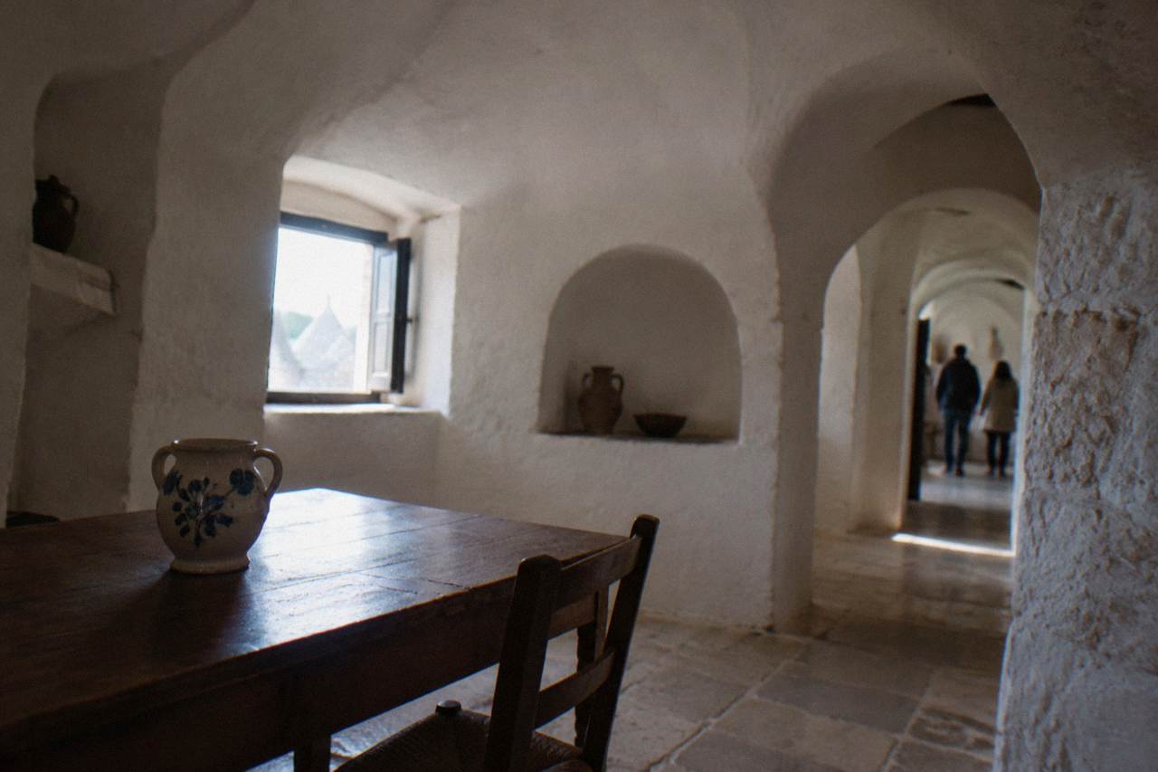 Whitewashed domed room with deep arched alcoves, a simple wooden table and a ceramic jug
