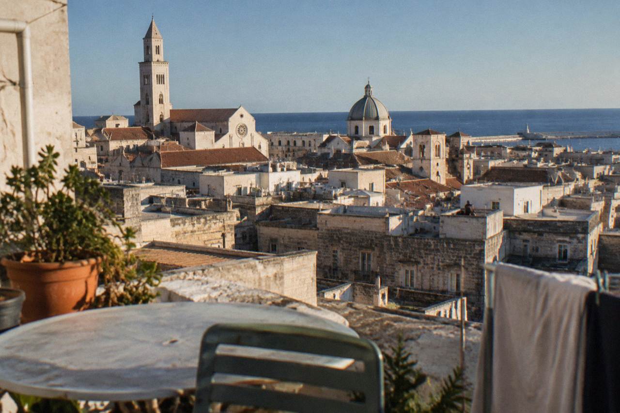 Terracotta and limestone rooftops and church domes of a dense old town seen from a high terrace with the sea beyond