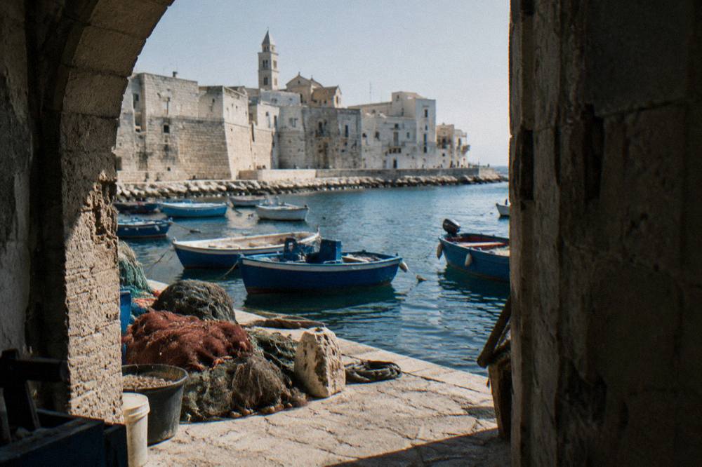 Small wooden fishing boats rocking at moorings with a net heap on the quay and pale old town walls behind