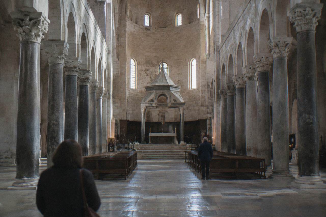 Long stone nave of a Romanesque basilica with simple columns and a raised sanctuary in soft window light