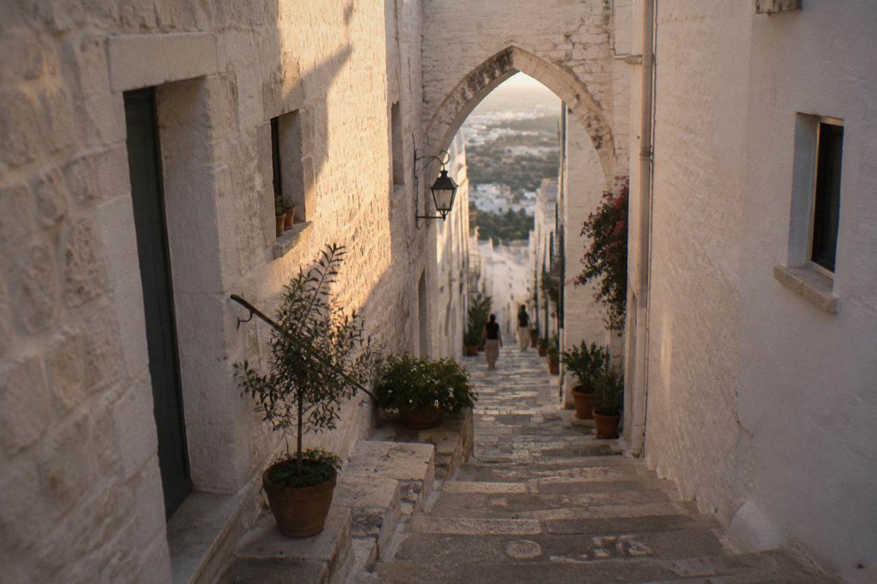Steep whitewashed alley with stone steps, a pointed arch overhead and potted plants