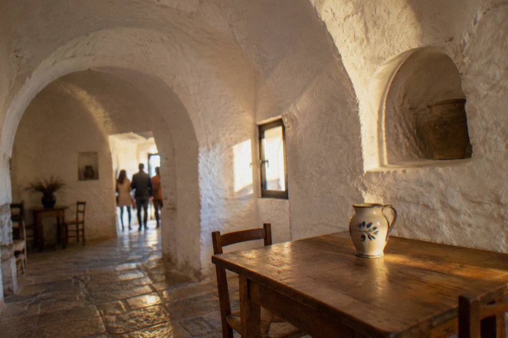 Whitewashed domed room with deep arched alcoves, a simple wooden table and a ceramic jug