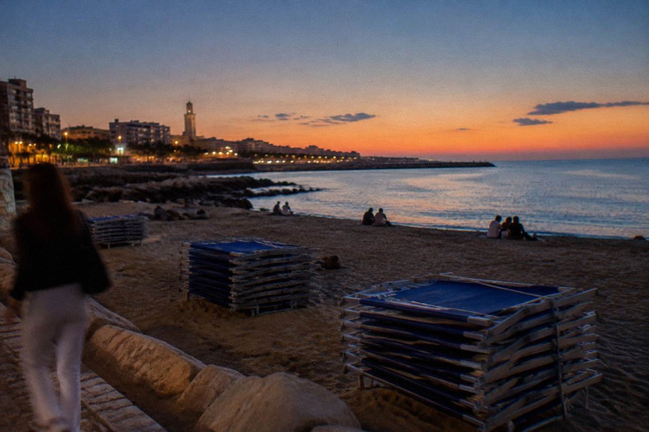 City beach in the evening with distant people on the sand, stacked sunbeds and an almost still sea