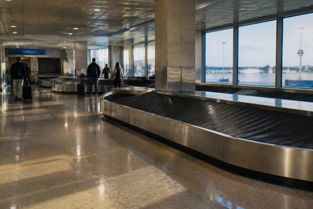 Baggage reclaim hall with an empty belt curving through and a few travellers watching far off