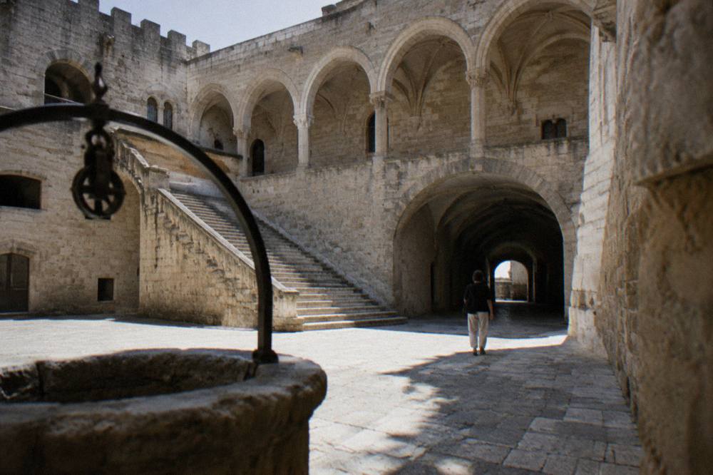 Inner courtyard of a medieval castle with a pale stone arcade, a broad staircase and a vaulted passage