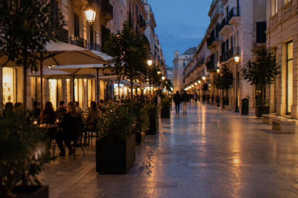 Pedestrian shopping street in the evening with lit lamps, cafe tables and out-of-focus people