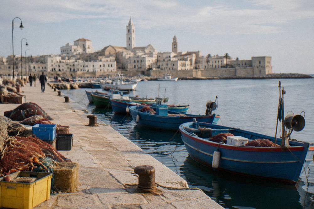 Old harbour pier with small wooden fishing boats, crates and nets and the pale old town skyline with two towers behind