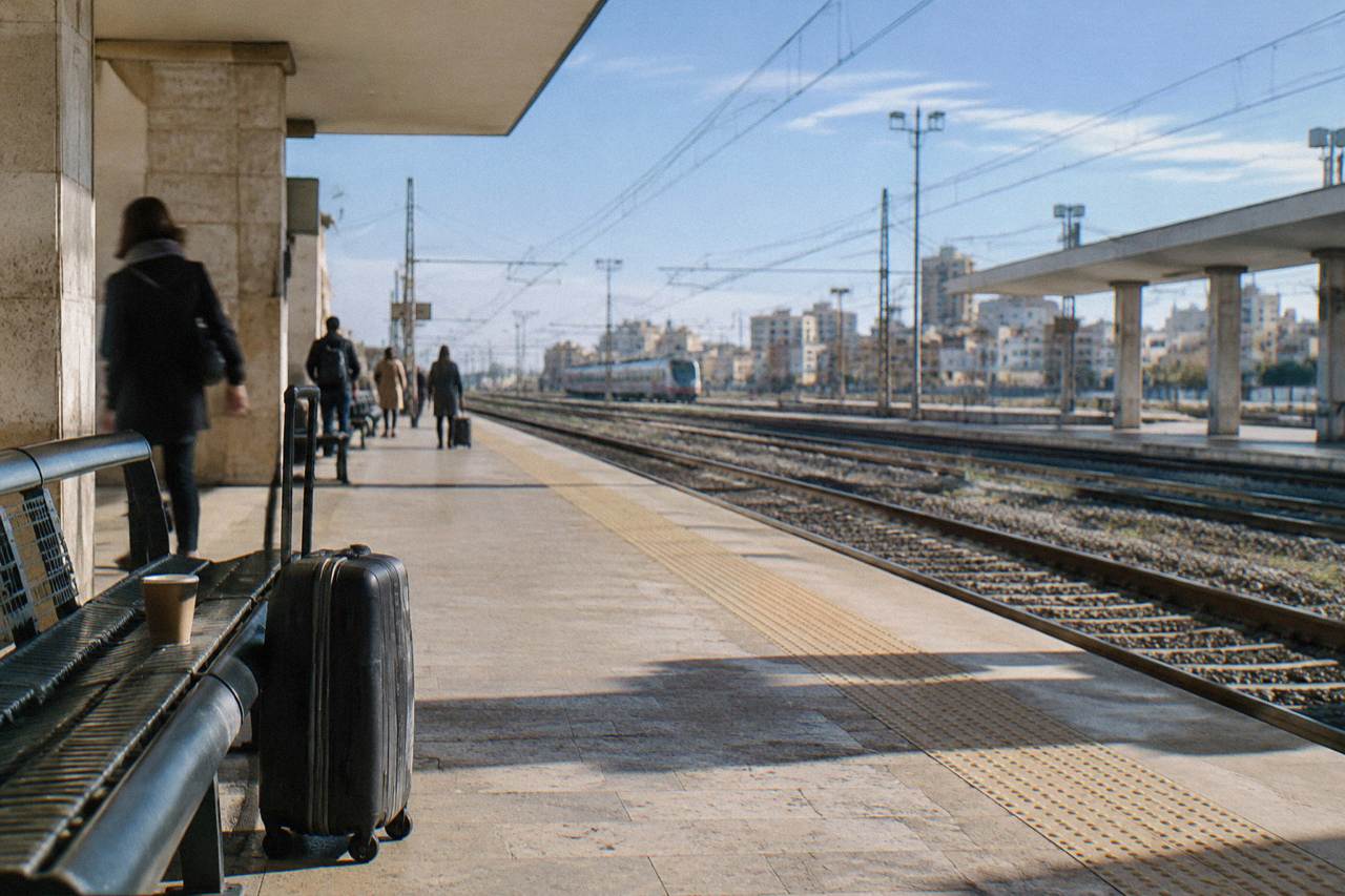 Platform bench with a suitcase and a paper cup beside empty tracks and a distant plain train