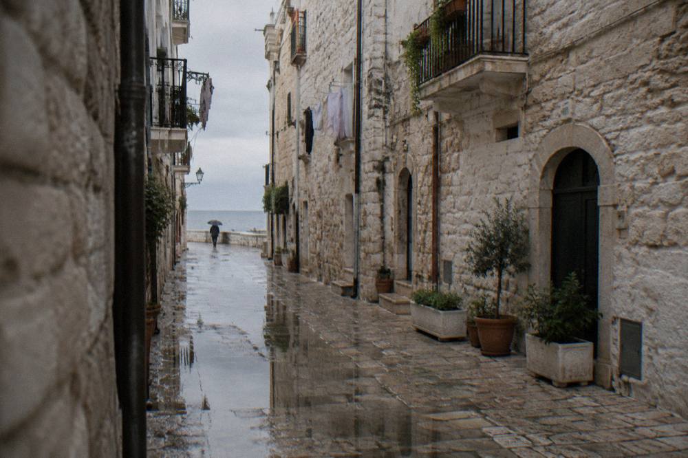 Wet limestone old town lane after rain with reflections in puddles and a distant person under an umbrella