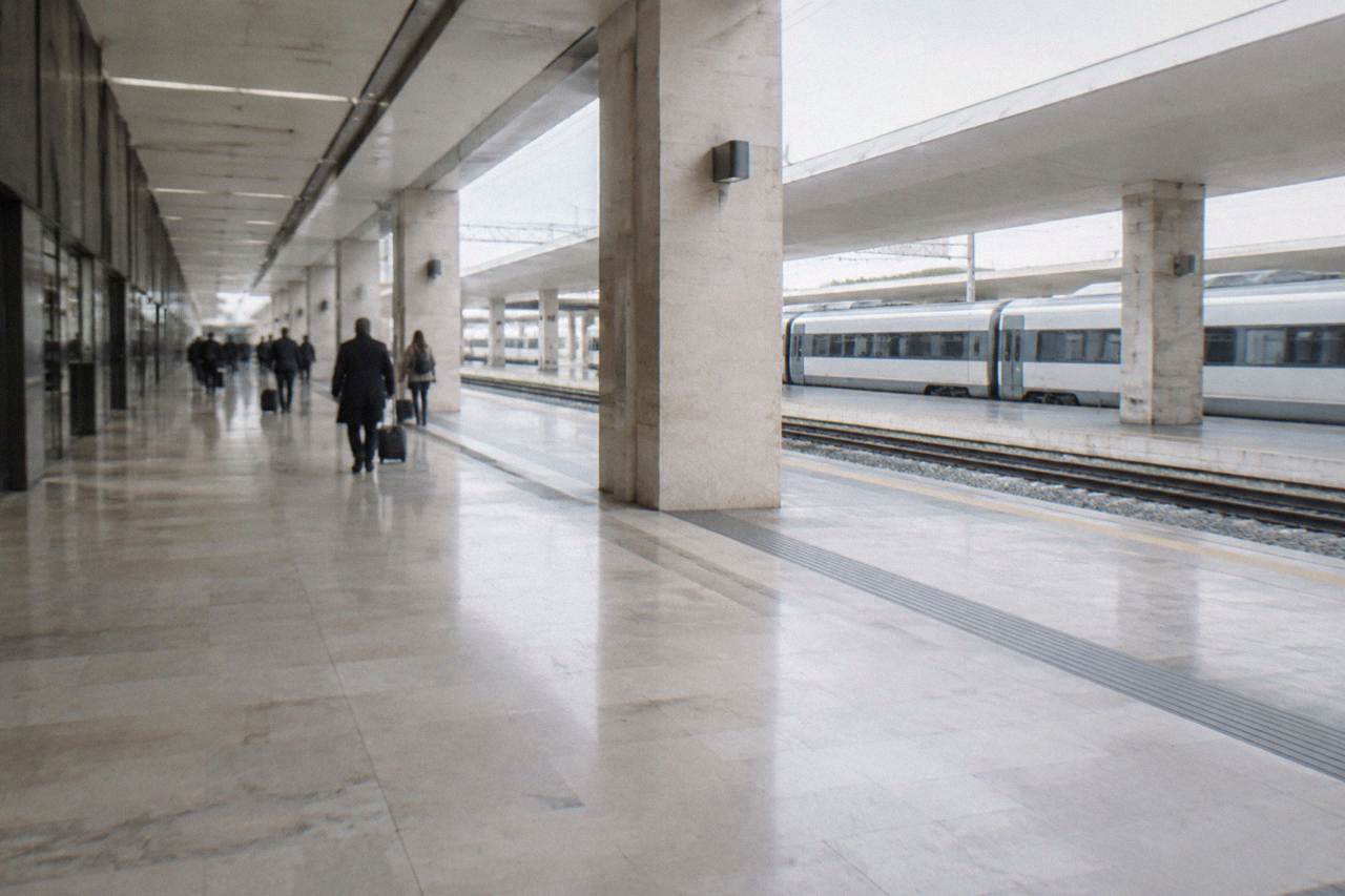 Large pale railway station with a long concourse, distant travellers with suitcases and plain trains at the platforms