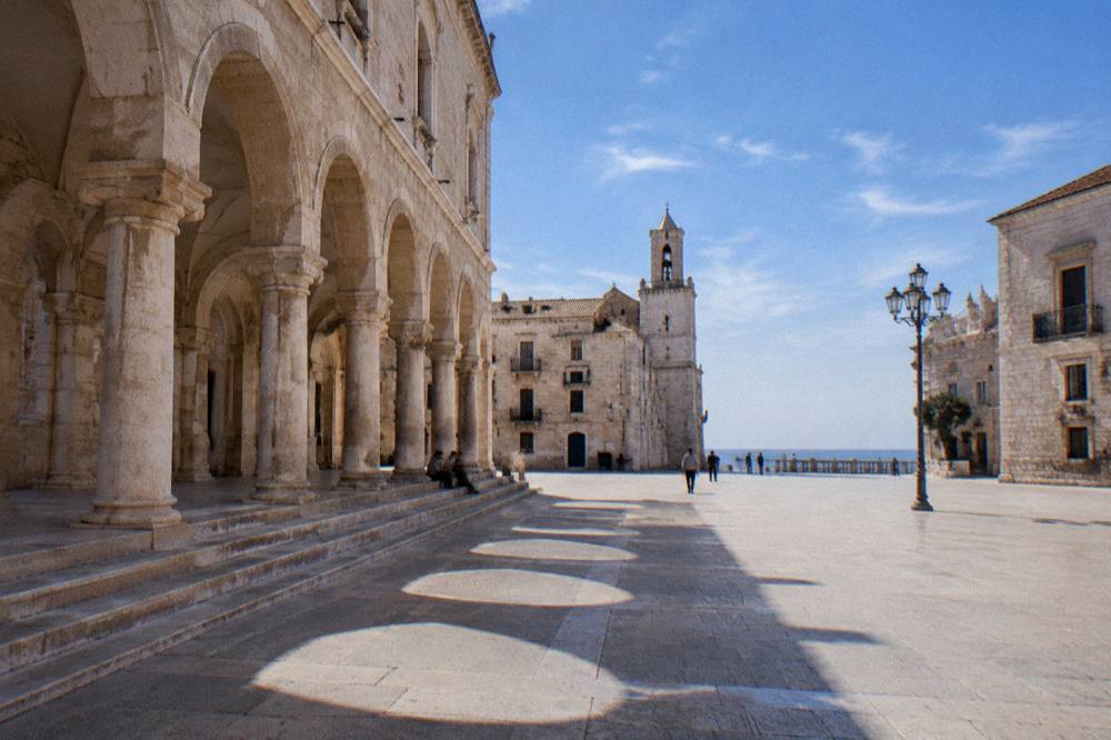 Loggia arches with long afternoon shadows and a few distant people sitting on the steps