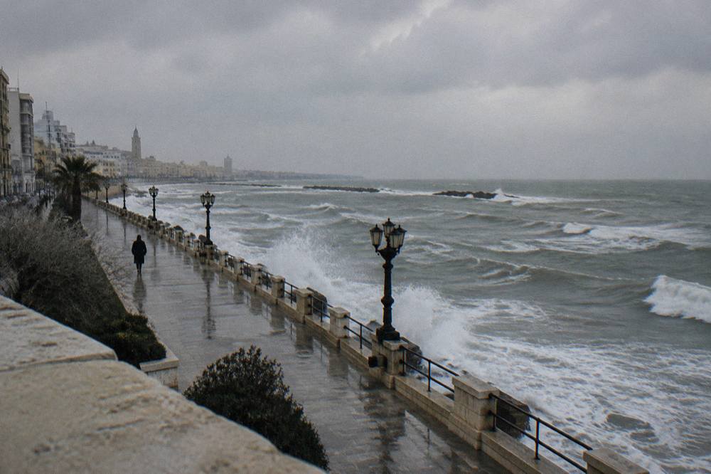 Grey winter sea with white-capped waves breaking against a seafront wall under a heavy sky