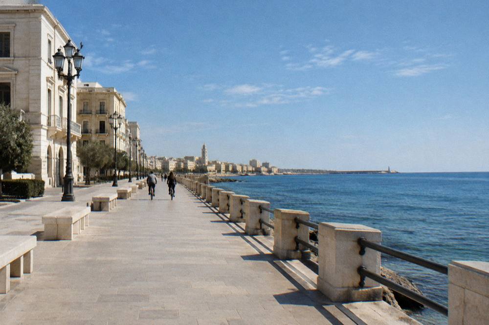 Cyclists far off passing stone benches on a promenade between cream monumental buildings and the calm blue sea