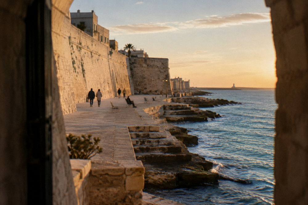 Massive pale limestone sea wall with a promenade at its foot and worn steps down to the water in low afternoon sun