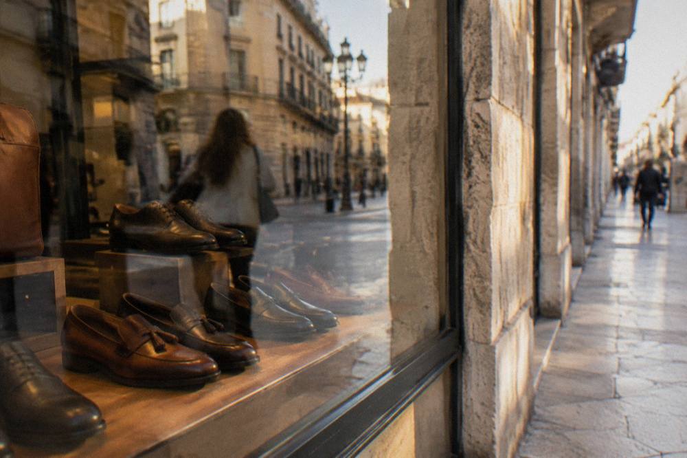 Shop window with leather shoes behind glass reflecting the street and a blurred passer-by