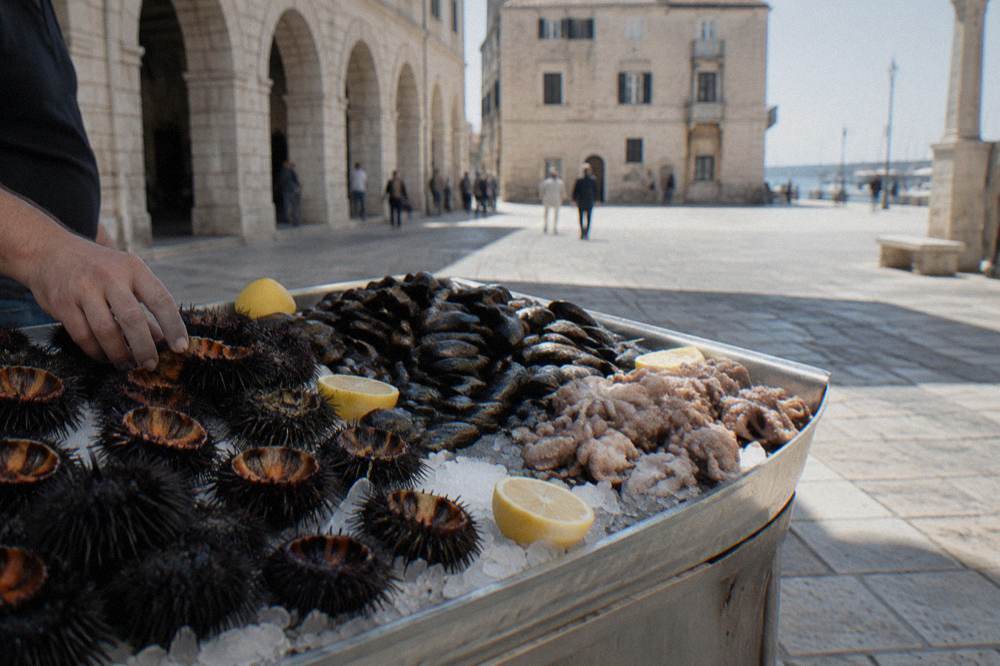 Fresh sea urchins, mussels and small octopus on crushed ice with lemon halves on a stone market counter