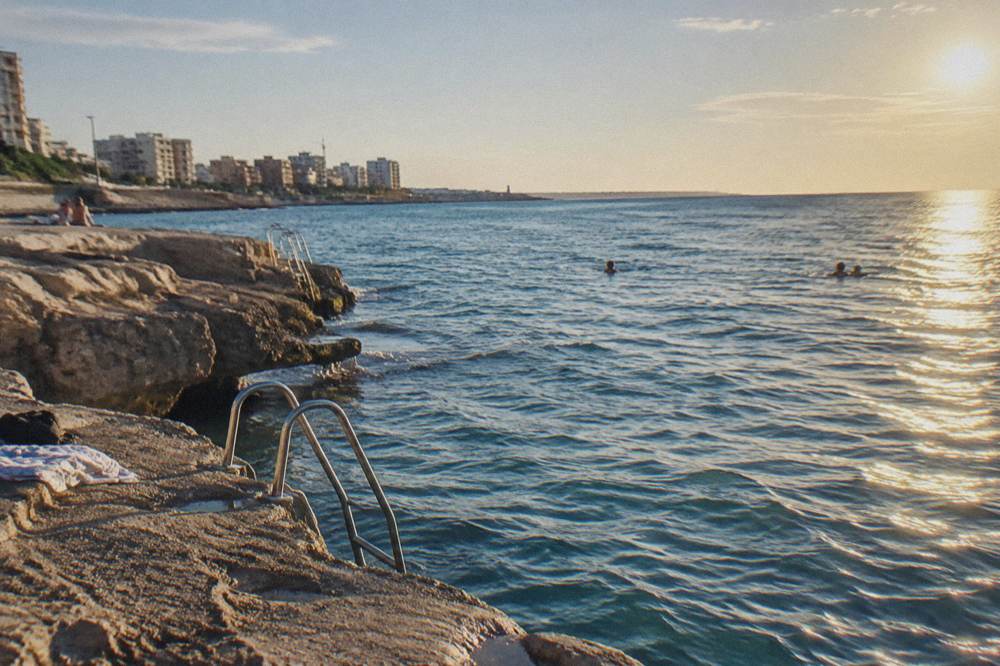 Small rocky bathing spot with ladders into the sea and a few distant swimmers