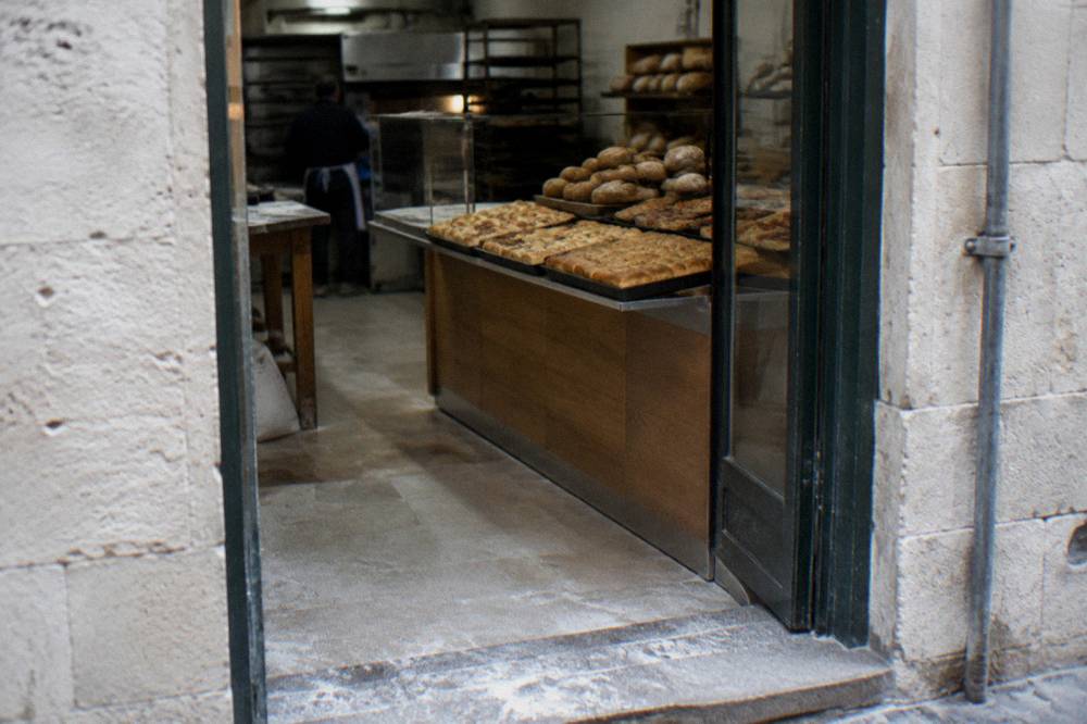 Neighbourhood bakery doorway with trays of golden focaccia and round loaves seen from the street