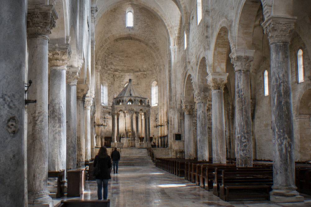 Long stone nave of a Romanesque basilica with simple columns and a raised sanctuary in soft window light