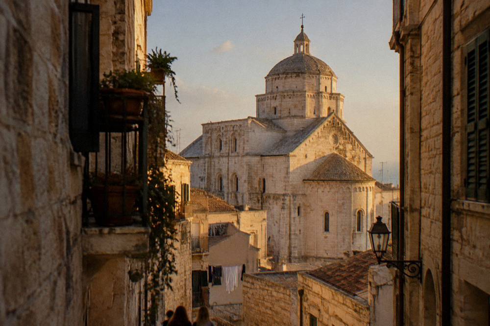 Cathedral dome and apse rising above terracotta rooftops at the end of a narrow old-town lane in afternoon light