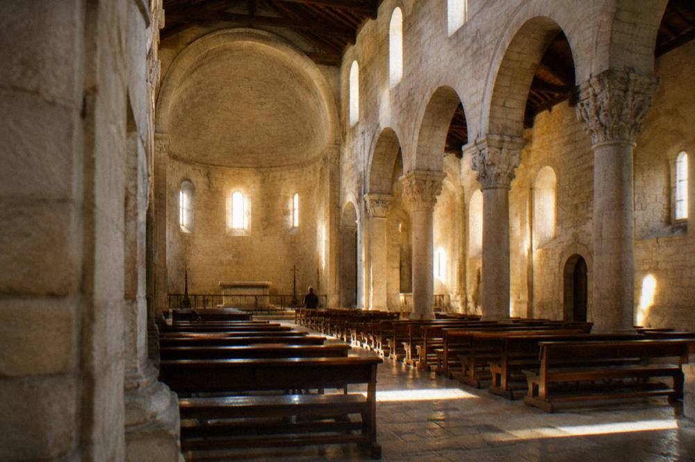 Bare stone cathedral interior with round arches, a high apse and shafts of light from small windows