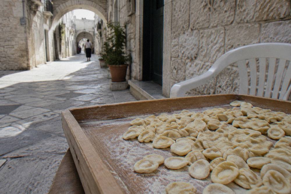 Tray of small ear-shaped orecchiette dusted with semolina on a wooden table beside a plastic chair
